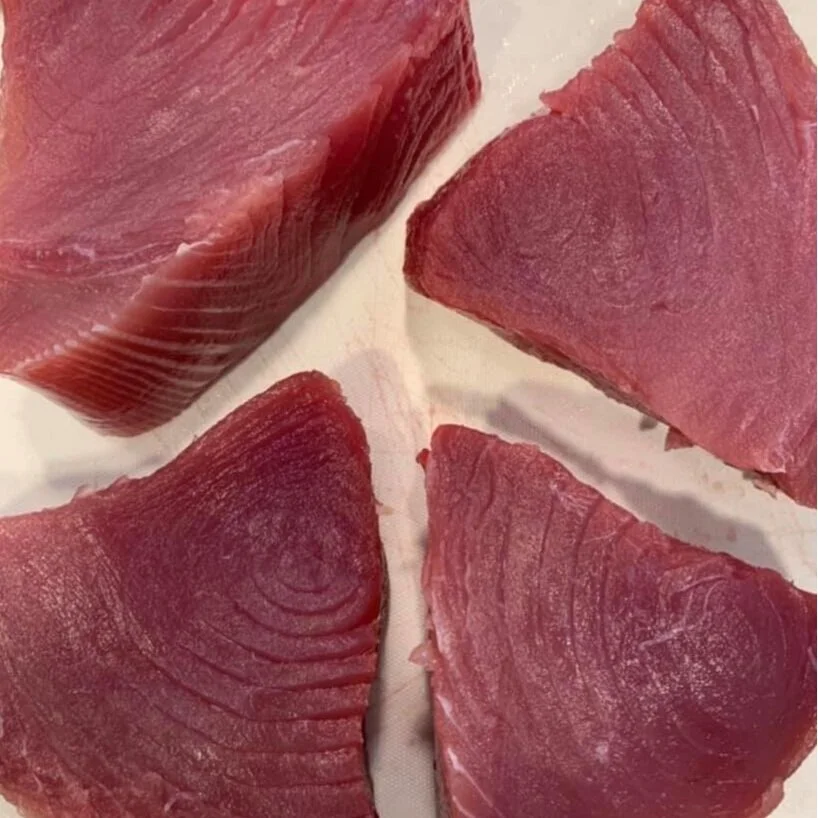 209558647_342552887452911_3299194361502951148_n Fresh cuts of raw tuna steaks arranged on a white surface, showcasing their vibrant pink color and smooth texture, ideal for sushi or grilling.